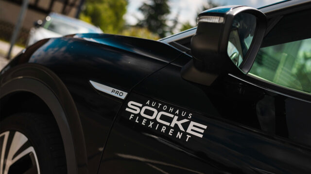 Nahaufnahme des Logos "Autohaus Socke Flexirent" an der Seite eines schwarzen Autos.