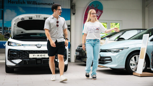 Eine Kundenberaterin führt einen Kunden in der Autohaus-Ausstellung vorbei an verschiedenen Fahrzeugen.