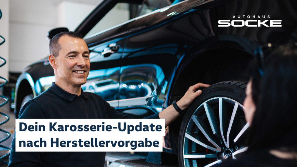 Karosserie- Update nach Herstellervorgaben. Socke Mitarbeiter steht lächelnd in der Werkstatt neben einem Auto auf der Hebebühne