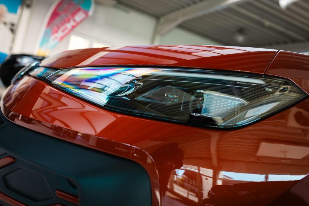 Nahaufnahme des modernen Frontscheinwerfers eines roten Volkswagen T-Roc mit regenbogenfarbenen Lichtreflexionen auf dem Scheinwerferglas.
