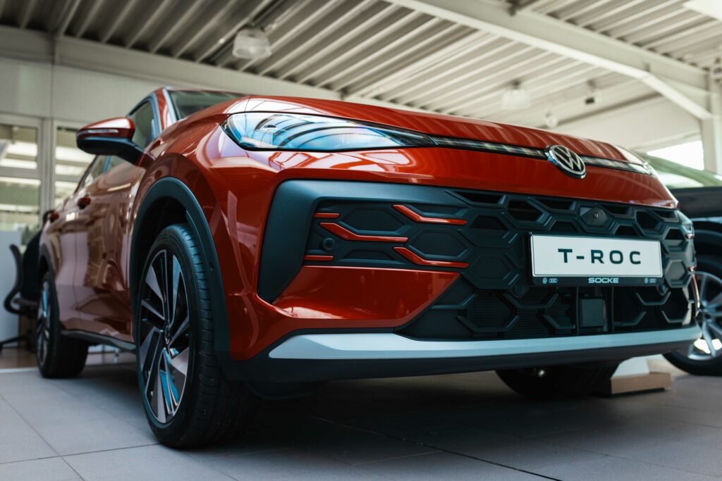 Froschperspektive auf das vordere Rad und die markante Seitenlinie eines roten VW T-Roc in einem Autohaus.