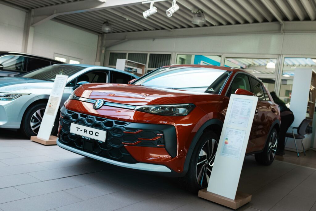 Die Fahrzeugfront eines roten Volkswagen T-Roc in der Ausstellungshalle eines Autohauses, im Hintergrund ist ein weiteres Auto zu sehen.