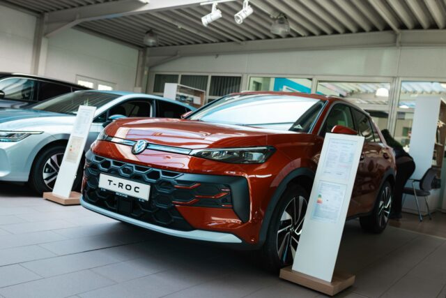 Die Fahrzeugfront eines roten Volkswagen T-Roc in der Ausstellungshalle eines Autohauses, im Hintergrund ist ein weiteres Auto zu sehen.