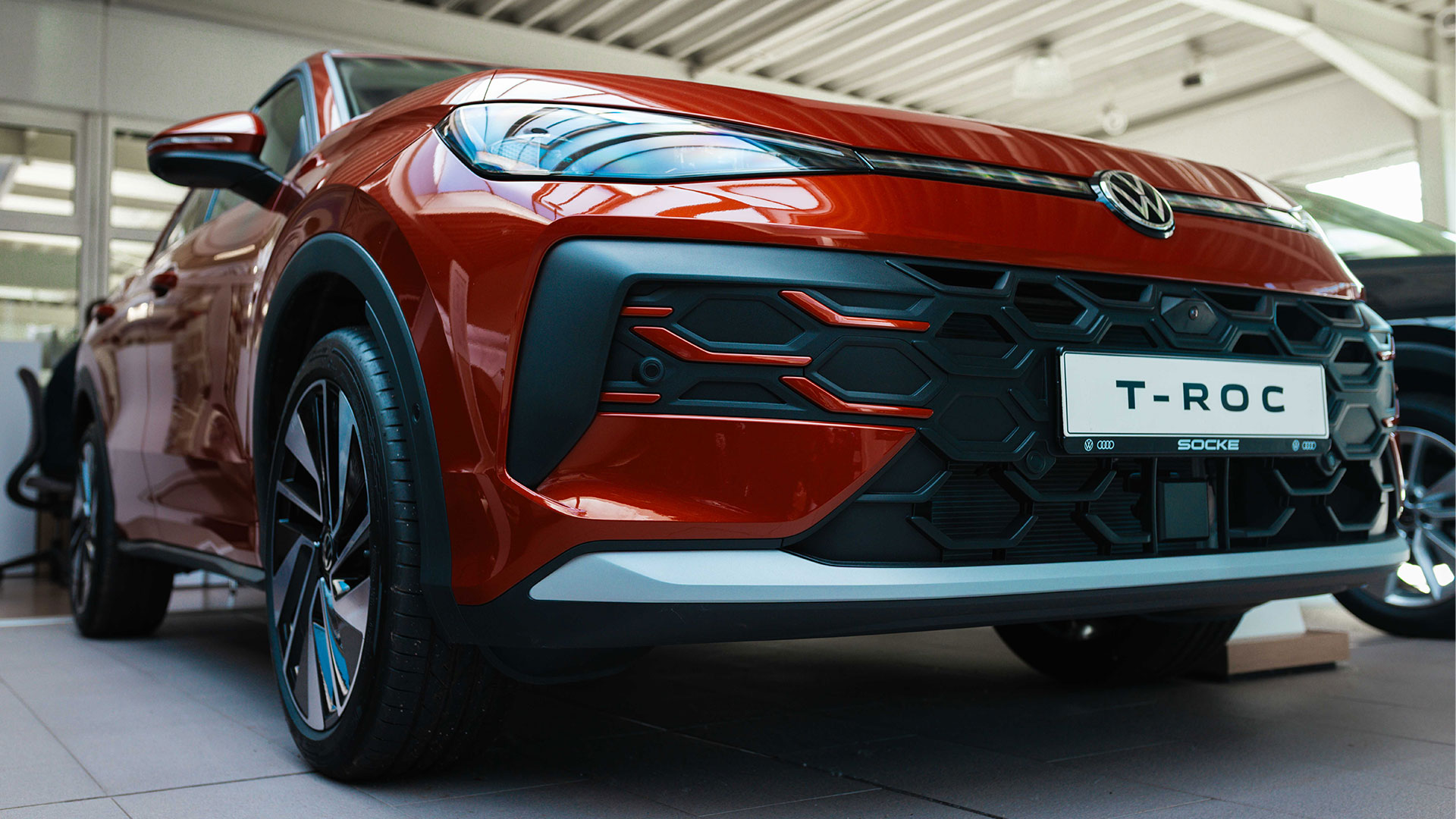 Froschperspektive auf das vordere Rad und die markante Seitenlinie eines roten VW T-Roc in einem Autohaus.