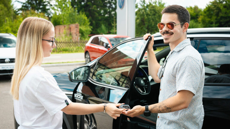 Socke Mitarebeiterin und ein lächelnder Kunde stehen vor dem gekauften schwarzen VW
