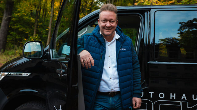Mitarbeiter von Autohaus Socke steigt aus dem VW Bulli aus und lehnt lässig an der Tür